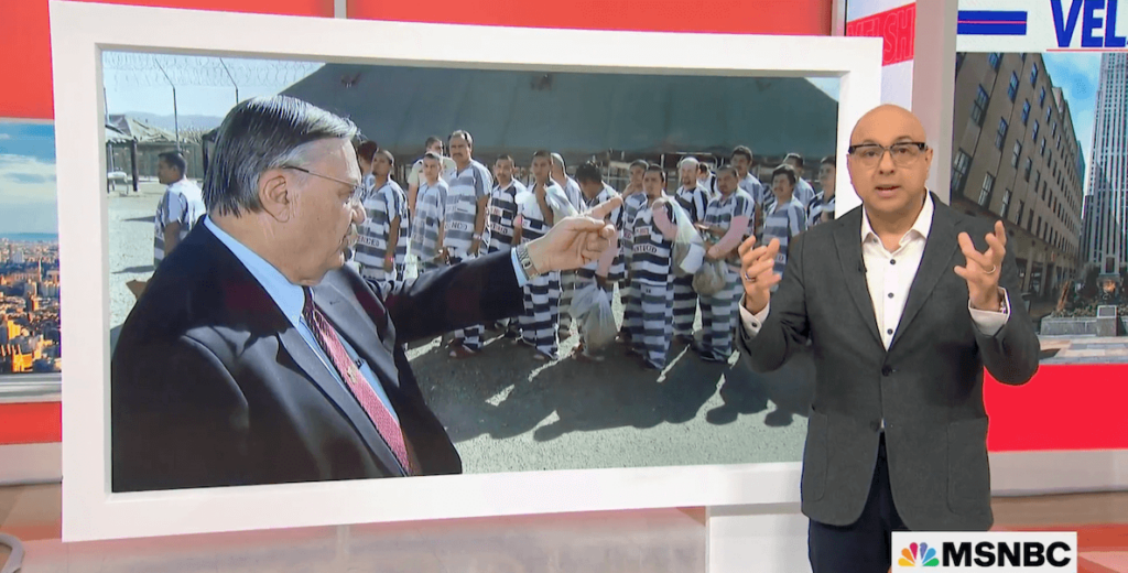MSNBC anchor Ali Velshi stands in front of a large photo of former Maricopa County Sheriff Joe Arpaio. Wearing a dark suit, Arpaio points toward a line of inmates wearing wide black-and-white striped jumpsuits and pink undergarments.