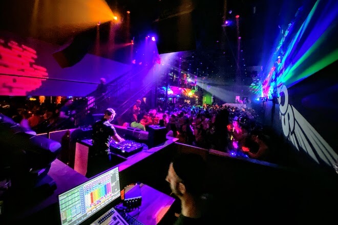 In a dark room, rainbow lights hit the ceilings, walls and dancers while a DJ spins at a Pride Philly Party.