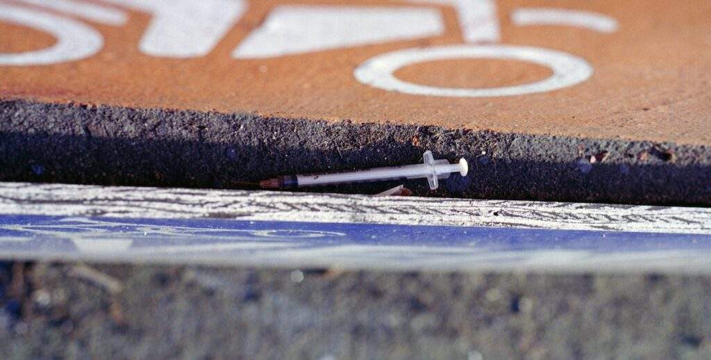 A used syringe lays between a cement curb and an orange bike lane in Vancouver, British Columbia.