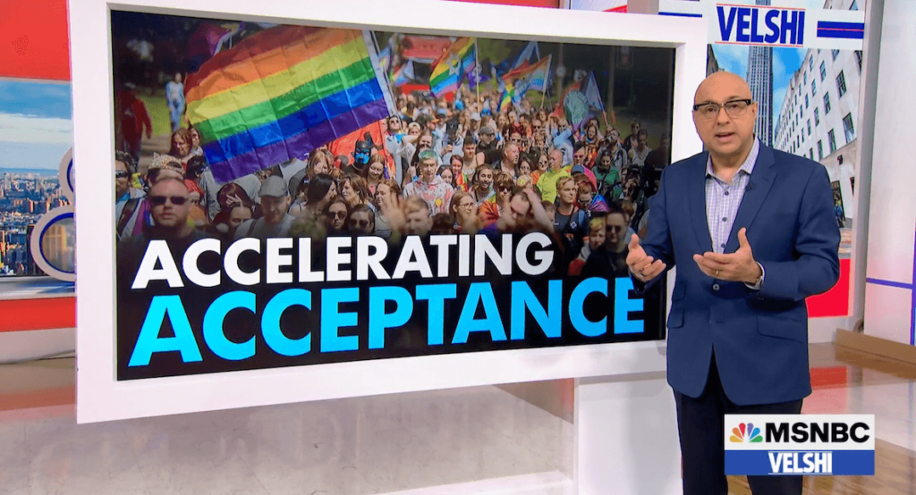 MSNBC anchor Ali Velshi stands in front of a screen displaying a Pride march and a large rainbow flag. The rubric "ACCELERATING ACCEPTANCE" appears beneath the image.