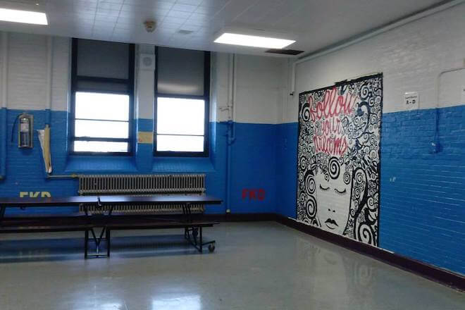 Inside Frankford High School in Philadelphia, a brick wall painted blue and white has a black-and-white mural of a woman with curly hair. Inside those curls is written in red cursive, "follow your dreams."