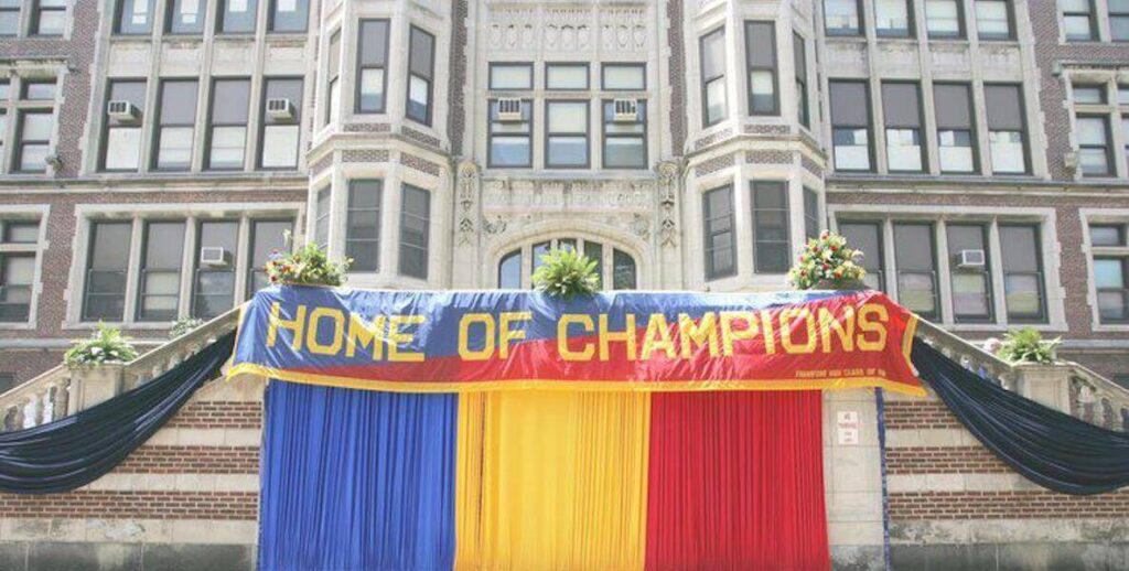 On the steps of circa 1914 Frankford High School in Philadelphia, a large blue, yellow and red banner reads "HOME OF CHAMPIONS."