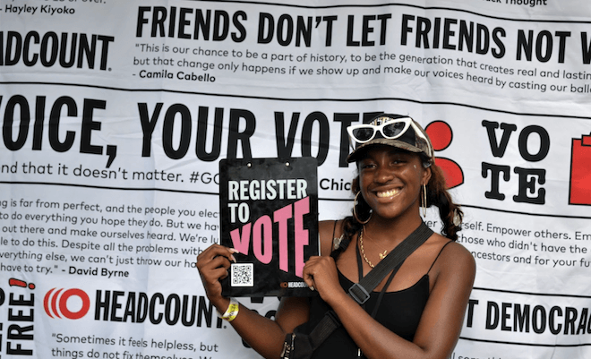 A volunteer from HeadCount, a national non-profit organization that works to register people to vote at music festivals, holds up a sign that reads, "REGISTER TO VOTE."