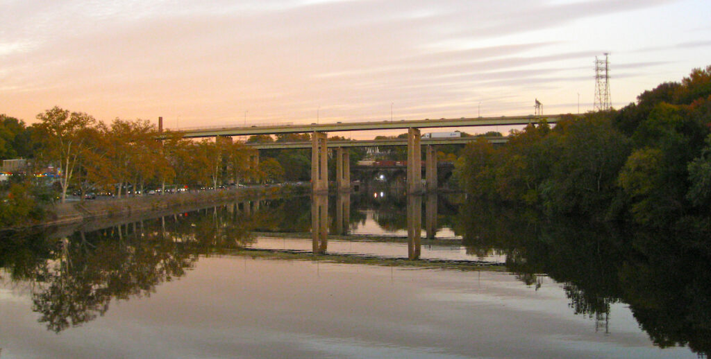 The Roosevelt Boulevard in Philadelphia includes a bridge that spans the Schuylkill River, which reflects the bridge at sunset.