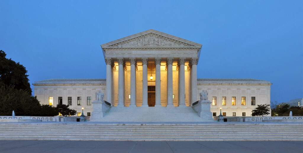 The United States Supreme Court, an imposing white marble building with a facade of eight columns, stands at dusk in Washington, D.C.
