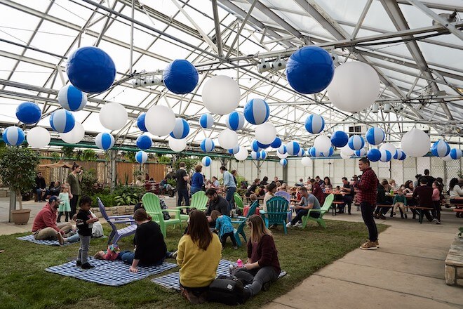 People sit on mats beneath blue and white beach balls inside the greenhouse of the Fairmount Horticulture Center.