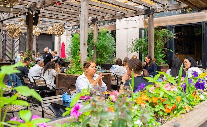 People sit at an outdoor restaurant beneath a slatted wooden ceiling at Harper's Garden in Philadelphia.