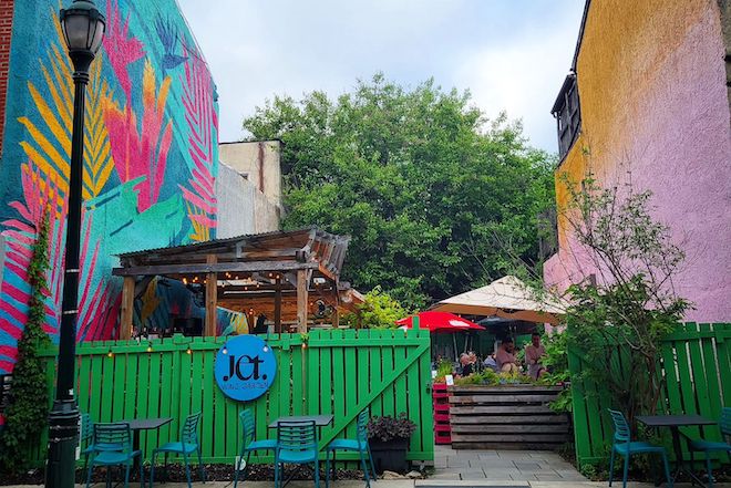 A green fence connects two brightly painted buildings on South Street in Philadelphia. Beyond the fence: the garden of Jet Wine Bar.