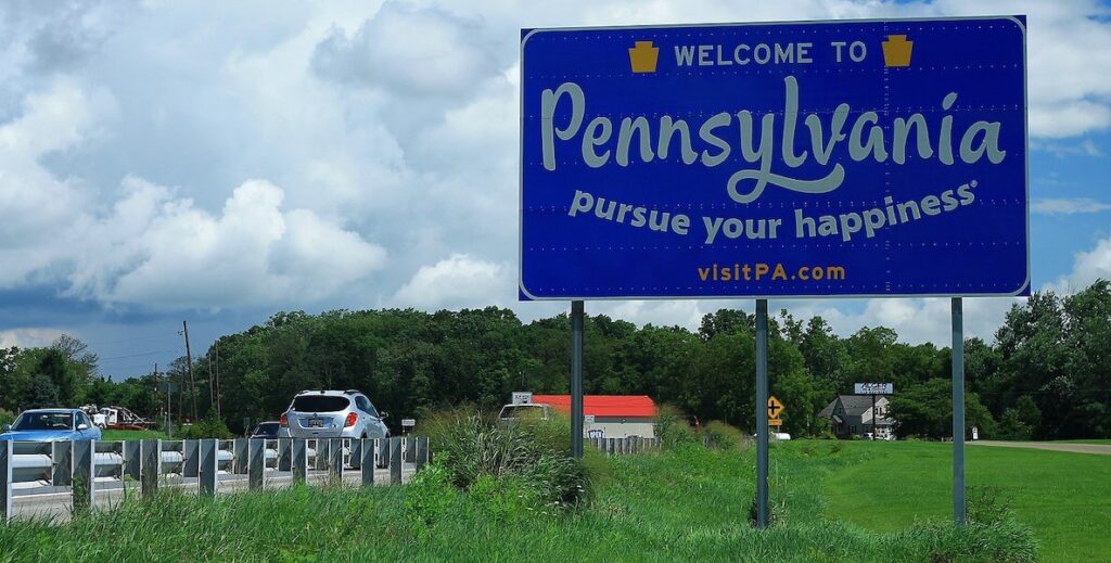 A roadside sign reads "Welcome to Pennsylvania. Pursue your happiness."
