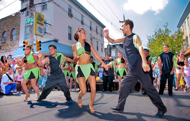 On N. 5th Street in Philadelphia, four dancers in black and green attire dance as part of Feria del Barrio, a celebration of Puerto Rican culture.