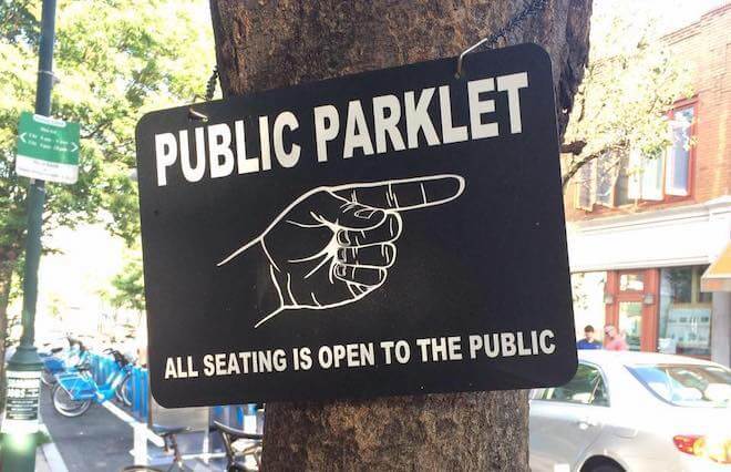 A black sign with white lettering reads "PUBLIC PARKLET" with a hand pointing to the right. 