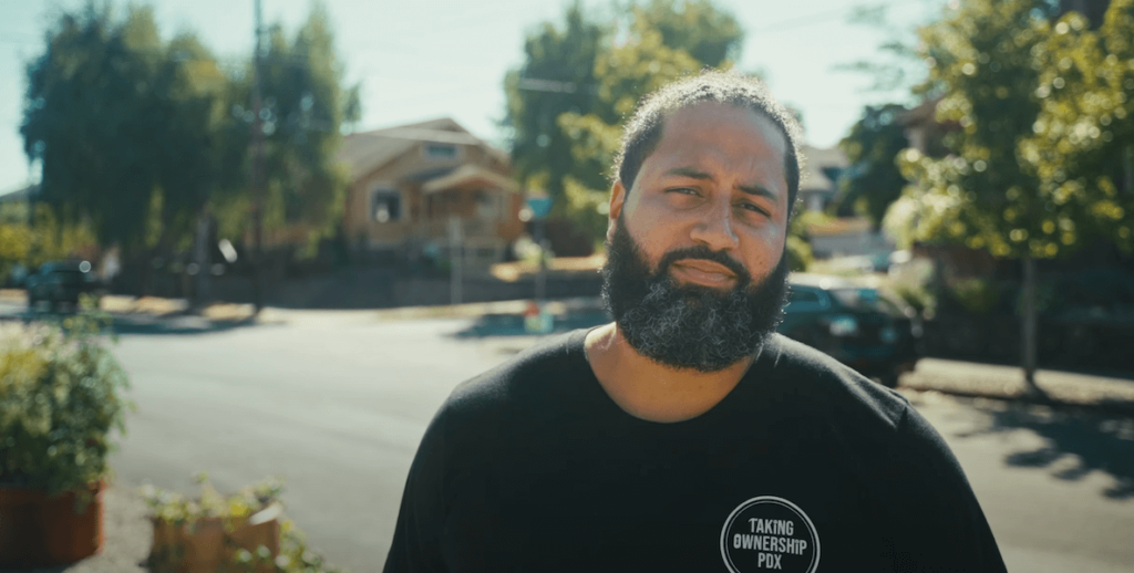 Randal Wyatt, founder of Taking Ownership PDX, is a Black man with a mid-length beard. He stands in what appears to be a residential neighborhood in Portland, where his organization works.