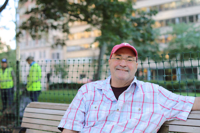 Doug Blonsky, a white man in a short-sleeved plaid shirt wearing a red cap, sits on a bench in Rittehouse Square.