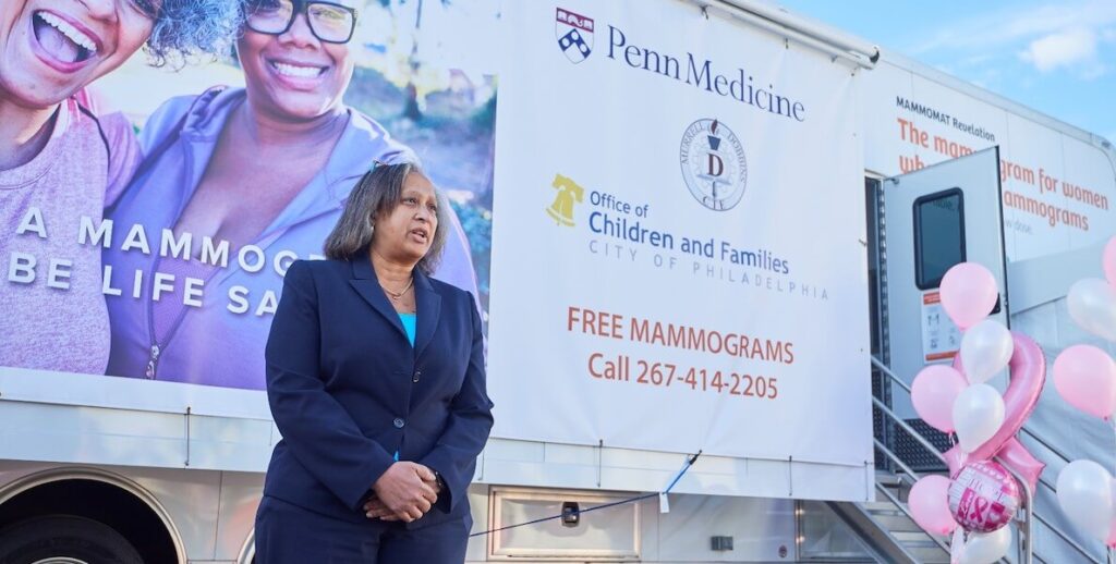 Dr. Nunes, a Black woman with shoulder-length grey hair, wearing a navy suit, stands in front of Penn Medicine's Mammogram van.