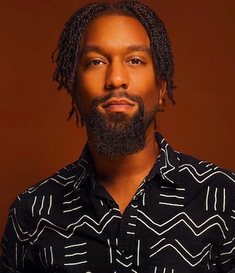 Portrait of Eric Cole, a Black man with ear-length braids and a black-and-white shirt.