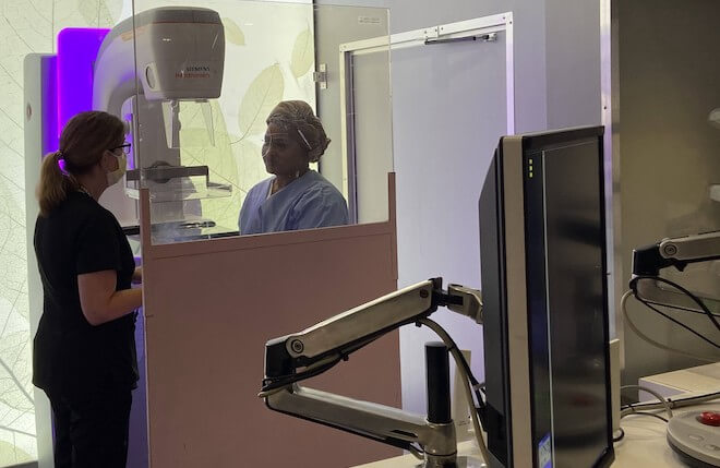 A nurse performs a mammogram on a patient. On view are the mammography machine and a monitor.