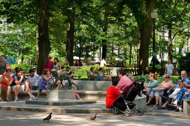 People sit on benches around a bronze statue of a goat. A child plays near the statue. This is Rittenhouse Square.