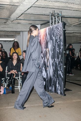 A model in a loose-fitting black satin menswear inspired suit walks the runway in a parking garage during Philadelphia Fashion Week.