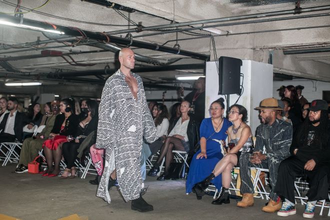 A male model in a sheer black-and-white caftan walks the runway in a parking garage during Philadelphia Fashion Week.
