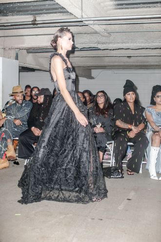 A model in a black gown walks the runway in a parking garage during Philadelphia Fashion Week.