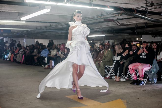 A model in an asymmetrical white satin gown walks the runway in a parking gage for Philadelphia Fashion Week.
