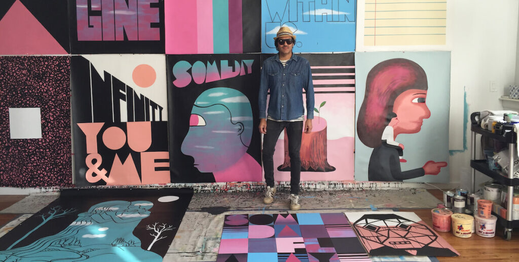 Jeremyville, a white male artist wearing all denim, sunglasses and a straw hat, stands in his Fishtown studio against and among his colorful paintings.