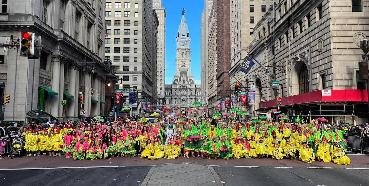 People dressed in bright yellow, green and hot pink dresses or "suits" represent the Two Street Stompers, a Philadelphia Mummers comic division, on Broad Street in front of City Hall.