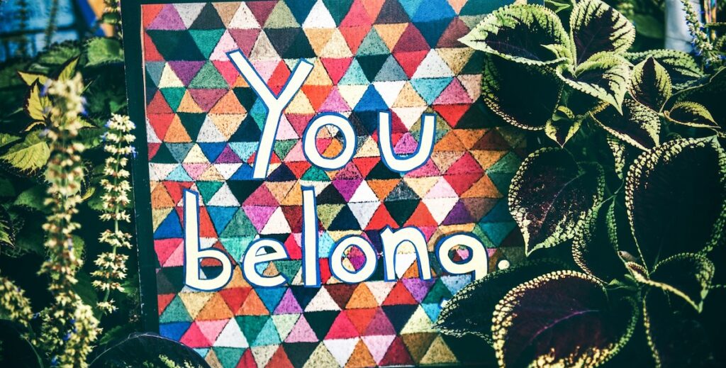 Betwen plants, a backdrop of different colored triangles bears the message "You belong."
