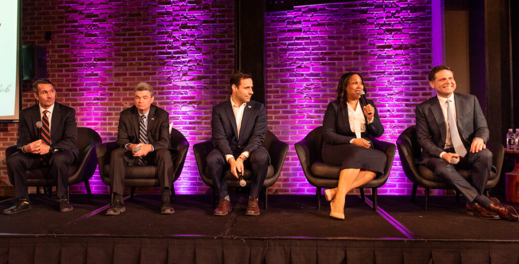 Attorney General candidates, l-r: Eugene DePasquale; Jack Stollsteimer; Joe Khan; Keir Bradford-Grey; and Jared Solomon sit on a stage before a purple lit brick wall. Photo by Germal Pleasant