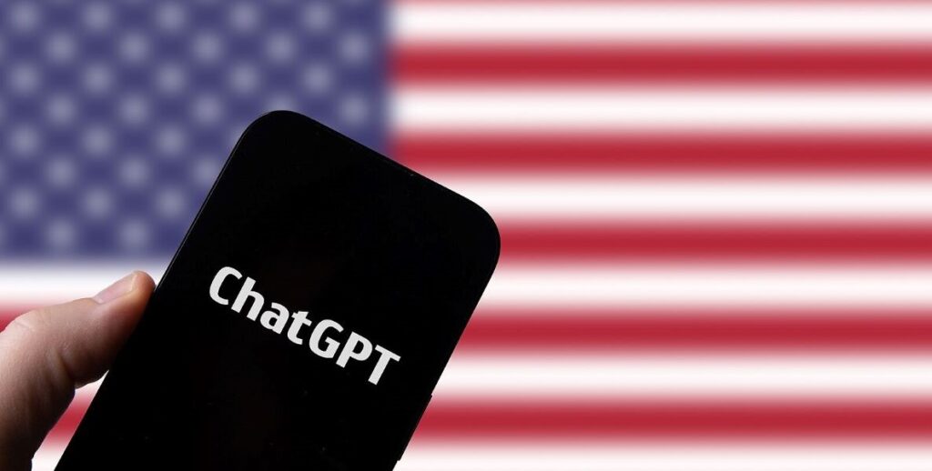 A mobile phone displaying ChatGPT is held up in front of an American flag in the background