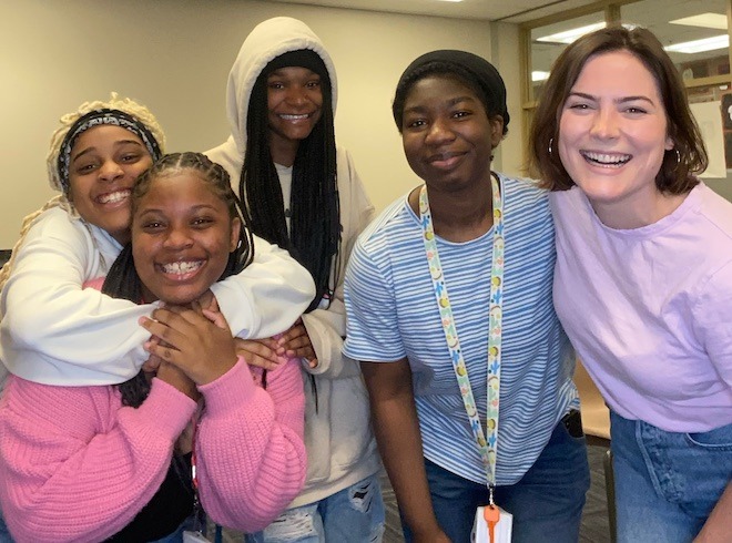 Four Black students, all young women, stand side by side smiling. Beside them is a a slightly older White woman, a facilitator for the Body Empowerment Project.