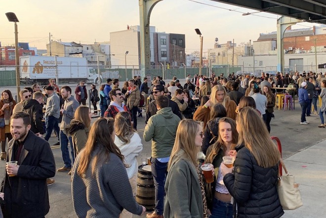 An Evil Genius block party is one of the things to do this week in Philly. Here, people stand outside, drinking beer under an overpass.