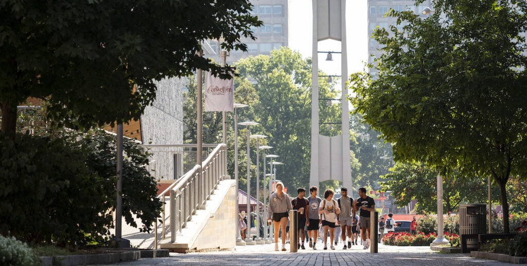 Students in shorts and t-shirts walk near the bell on the campus of Temple University.