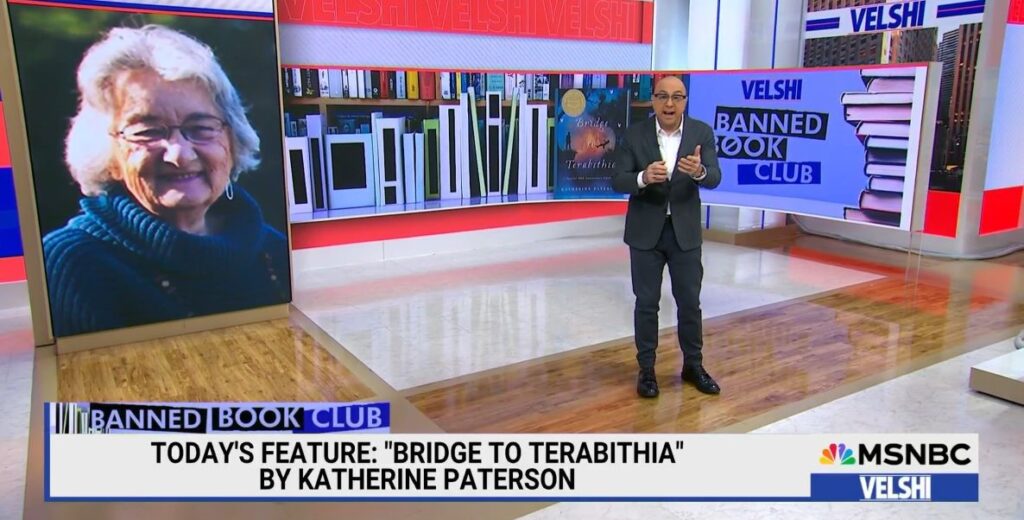 Ali Velshi stands on the set of his show in front of the cover of Bridge to Terabithia and a photo of Katherine Paterson to his left, who he is about to interview