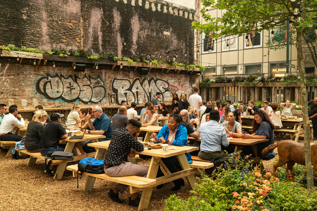 A number of people sit at picnic tables inside an urban beer garden in Philadelphia.