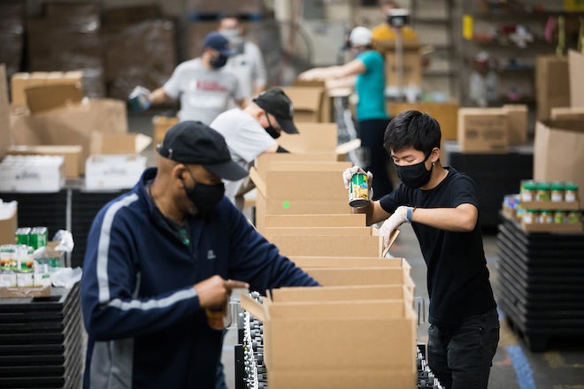 Workers stand on either side of a table full of cardboard boxes, filling them with food for Share Food, a Philadelphia non-profit.