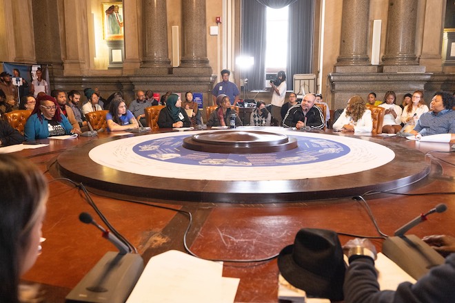 The People's Budget Roundtable — members of Philadelphia City Council and artists involved in the project sit around a large round table in a grand, columned room in Philadelphia City Hall. Photo by Steve Weinik for Mural Arts Philadelphia.
