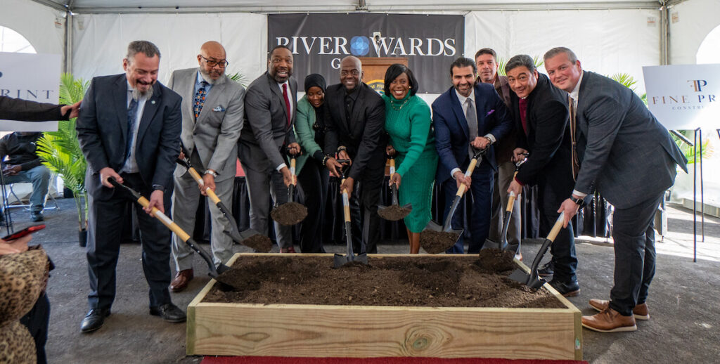 Philadelphia Mayor Cherelle Parker, an African American woman with bobbed hair wearing a green sweater dress stands in the center of a line of nie people, all men in suits except one woman in a hijab and green jacket and black dress, holding shovels over a wooden-framed patch of dirt at the River Wards groundbreaking and Turn the Key event.