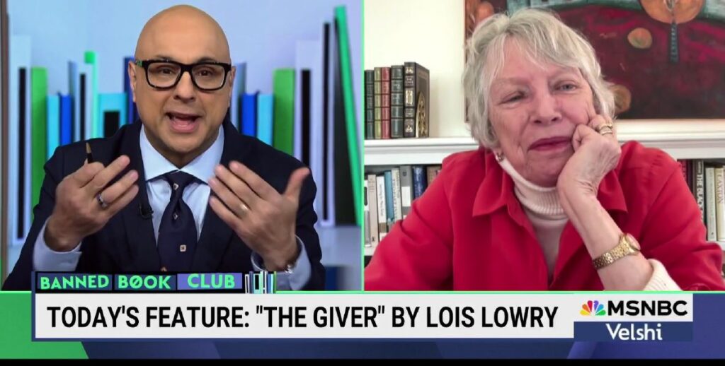 A split screen image shows Ali Velshi on the left, a bald Indian man wearing a suit jacket, blue shirt and tie and glasses, speaking with his hand raised. To the right, The Giver author Lois Lowry, a White woman with short grey and white hair, a red collared shirt over a white turtleneck backdropped by books on a shelf.