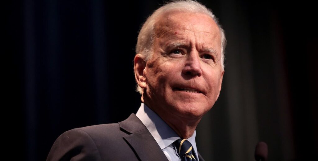 The head and neck of Joe Biden, a White man with white hair, wearing a suit.