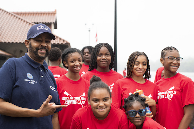 District 4 Councilmember Curtis Jones Jr. (far left) stands alongside middle-school-age girls wearing matching red t-shirts. They are all African American.