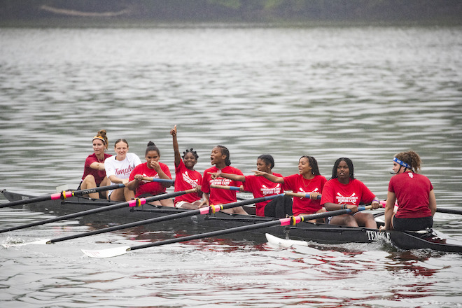 Middle school students in bright red t-shirts row in Temple boats along the Schuylkill River.