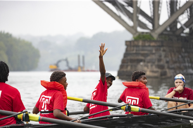 Middle school students in bright red t-shirts row in Temple boats along the Schuylkill River.