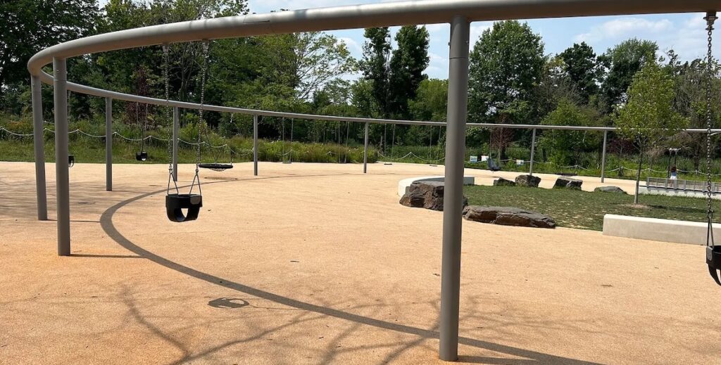 An empty swing set stands in nearly full sun at the newly built Anna C. Verna Playground in FDR Park in Philadelphia.