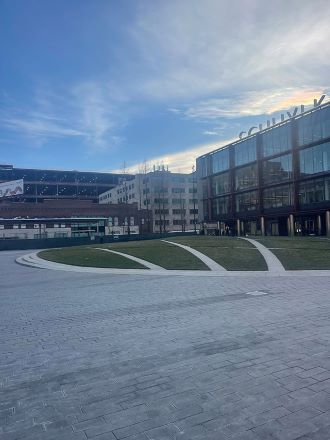 Grey asphalt in the foreground, a green yard in the background with the Schuylkill Yards glass facade and other buildings further behind