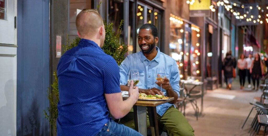 Two gentleman in casual clothes are socializing at an outdoor table on the sidewalk on 13th Street in Philadelphia