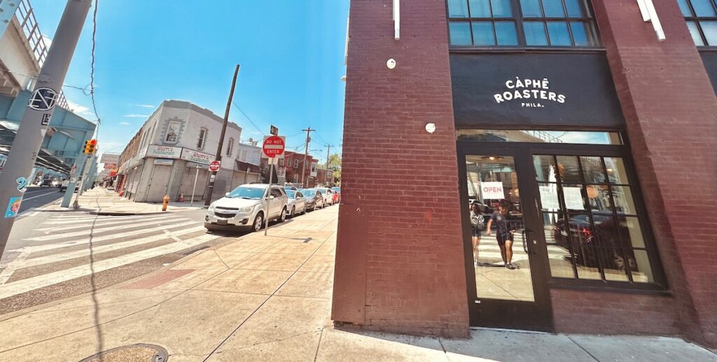 A brick building stands on a corner in the Kensington neighborhood of Philadelphia. Over the glass door entrance hangs a sign that says Càphê Roasters.