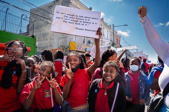 Philadelphia students — mostly Black children wearing red shirts; one carrying a sign with an Eleanor Roosevelt quote — take part in Peace Day Philly.