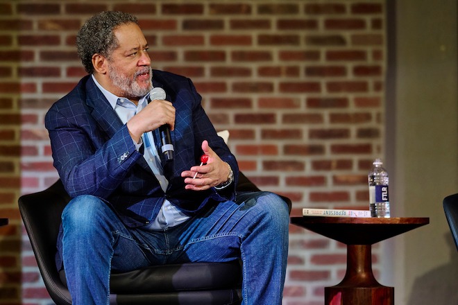 Michael Eric Dyson, an African-American intellectual and author, sits on a stage and speaks into a microphone.