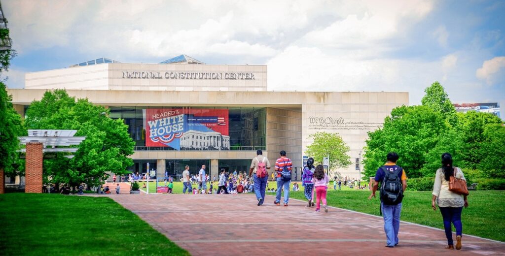 The National Constitution Center a museum in Old City, Philadelphia, stands at the end of a long pathway between green grass.